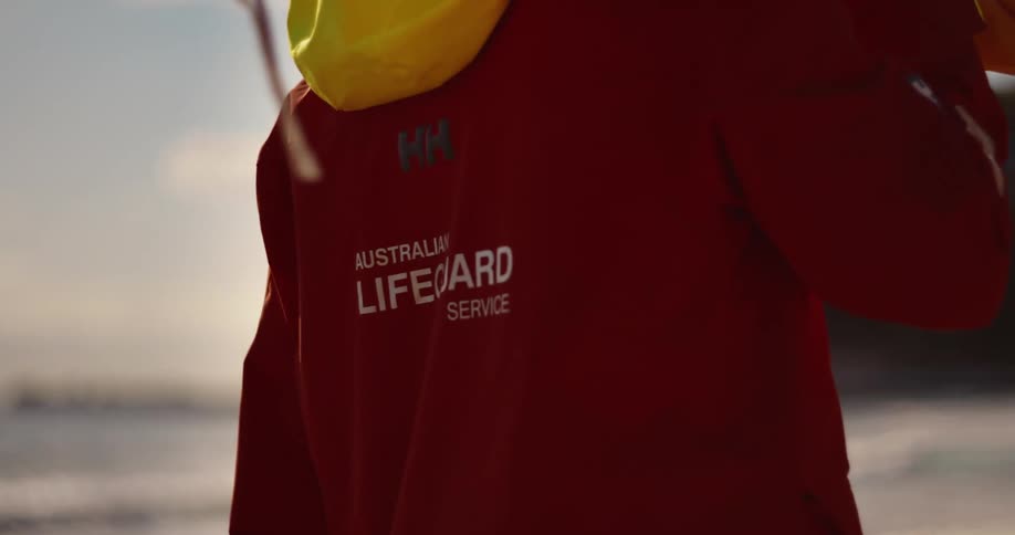 Close up of the back of a person walking in a red jacket on the beach