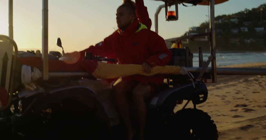 A lifeguard in red clothes is driving a small car on a beach in the sand