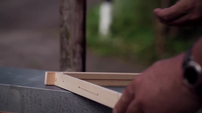 A helper holds the wood frame so pins can be hammered in