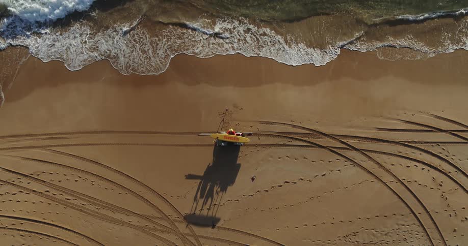 Lifeguards unloading yellow surfboards from a small vehicle near the coast