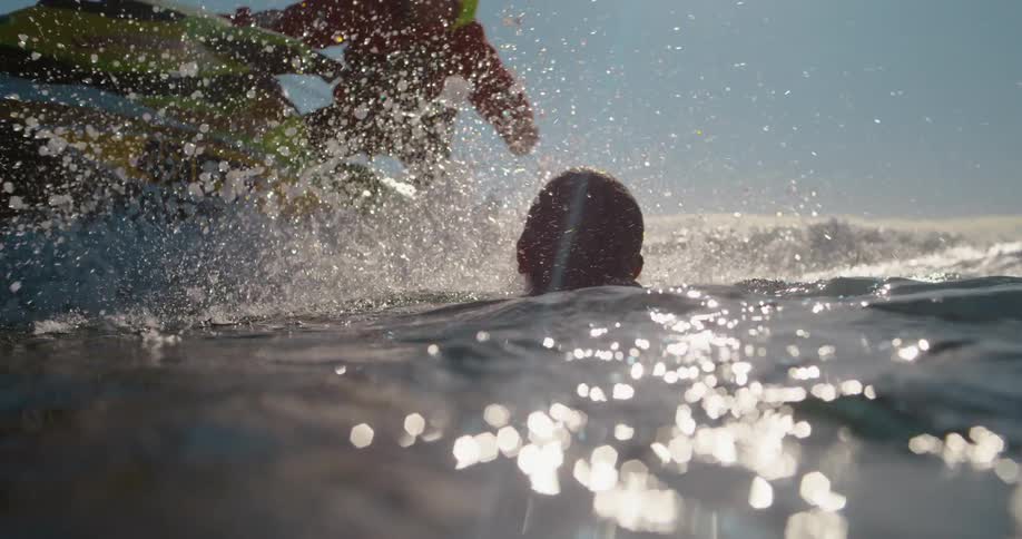 A person in a red jacket is helping a shirtless person out of the water onto a green and white jet ski