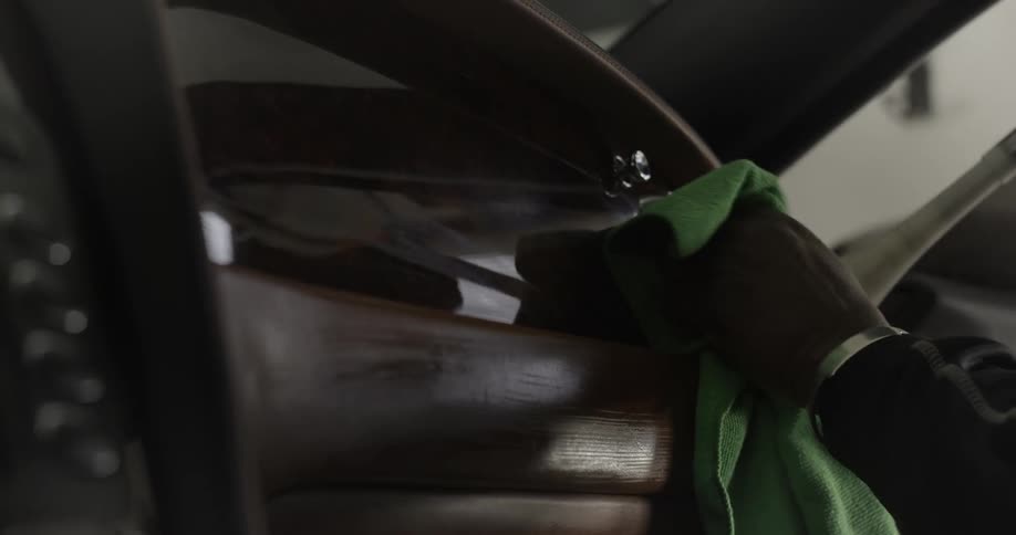 Hand holding a green cloth while cleaning a shiny wooden surface of a car