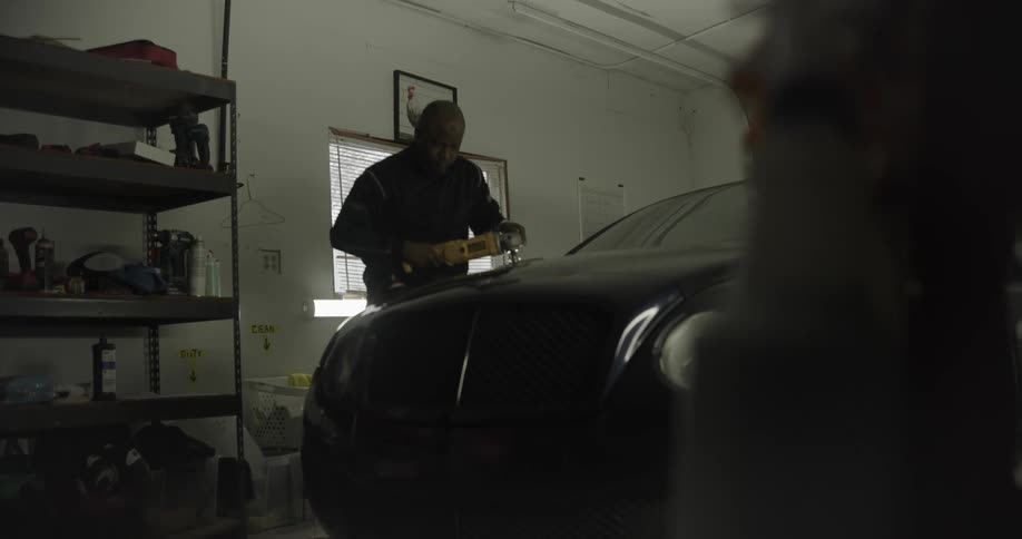 Man in a workshop polishing the hood of a black vehicle