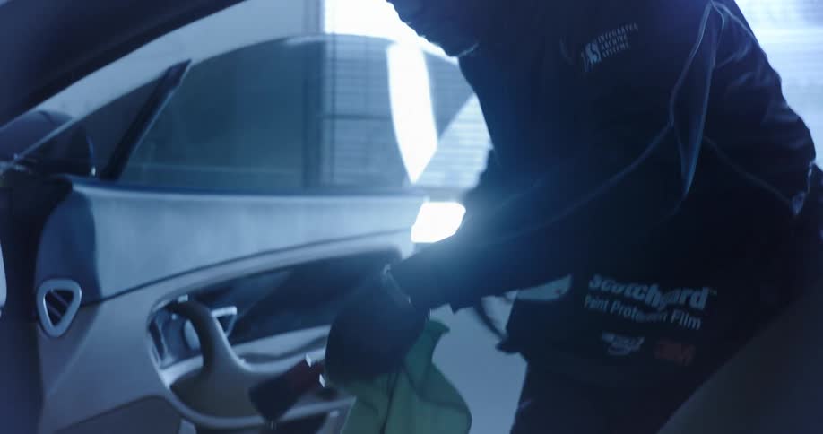 A person is cleaning the interior of a car near the drivers seat with a green cloth and a small brush