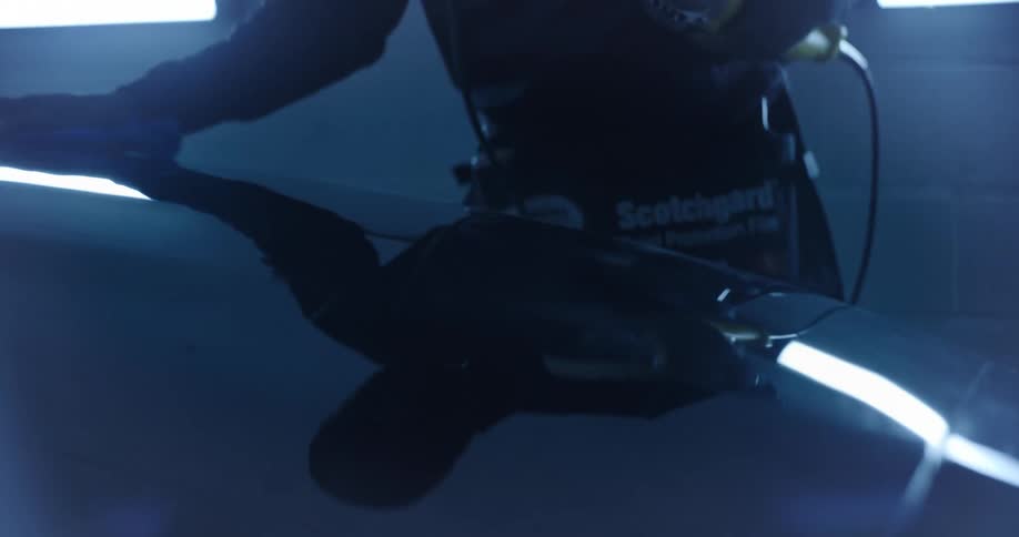 Professional applies protection to the paintwork of a car in an environment illuminated by blue light