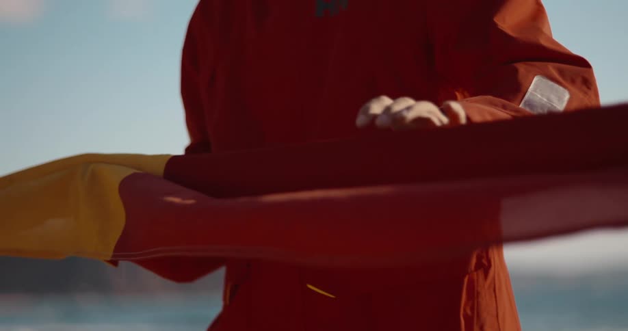 A person wearing a red jacket is holding and unfolding a yellow and red flag against a clear blue sky