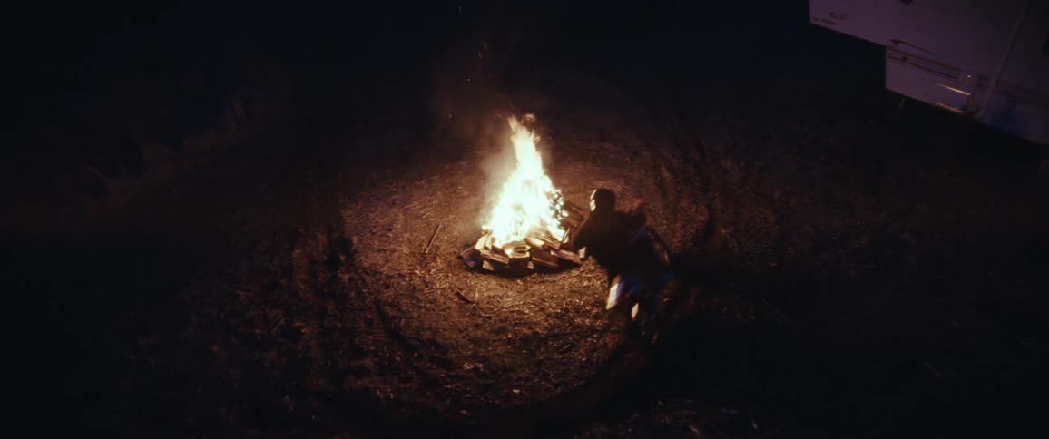 A person rides a motorcycle around a campfire at night