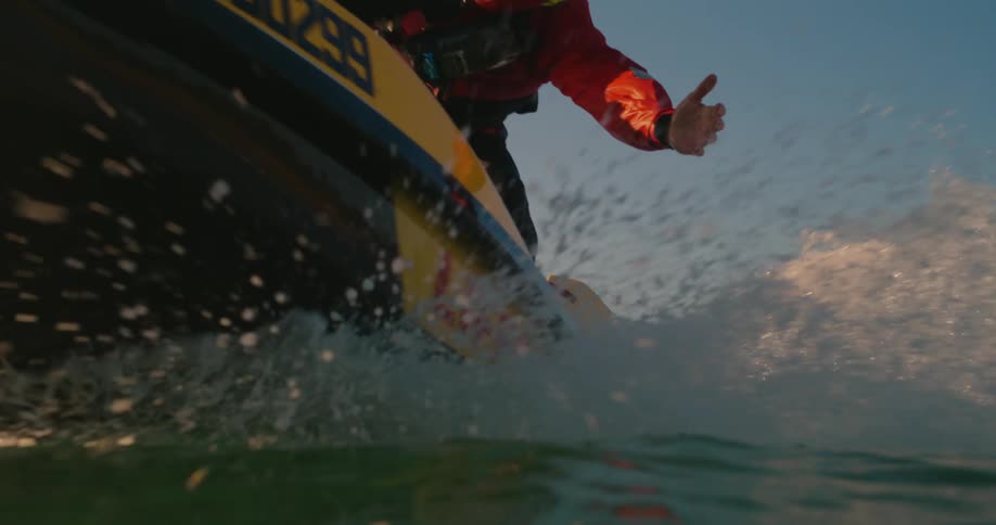 A person in a red jacket reaches into the ocean with an outstretched hand attempting to rescue