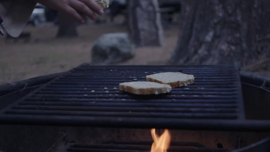 Person placing slices of bread on the grill with an open flame beneath