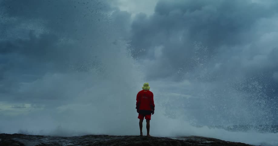 Waves crash around the man standing on the beach
