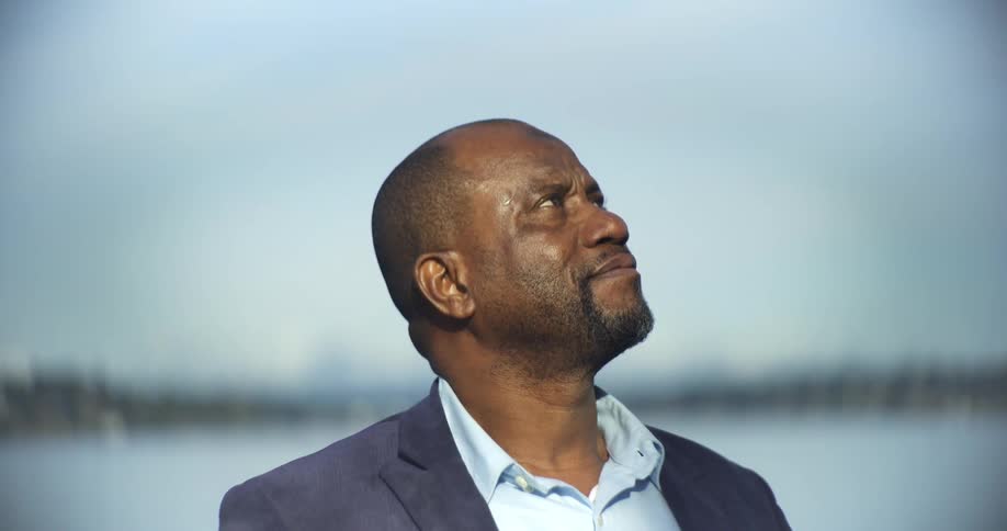 The face of a bald man who is turning his head to look up at an external beast he is wearing a blue suit