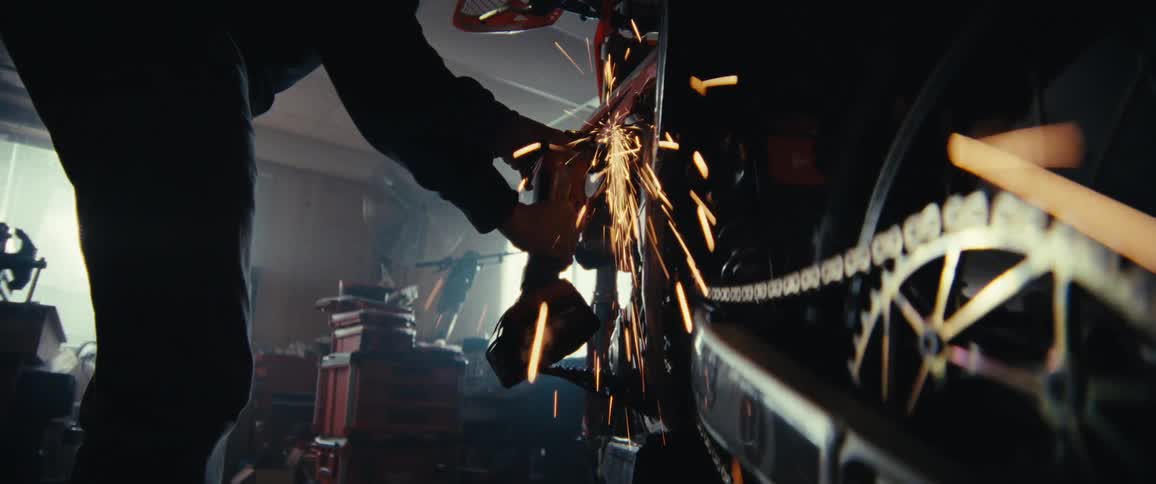 A person is using a power tool to grind or cut metal on a motorcycle causing bright sparks to fly in a workshop filled with various tools and equipment