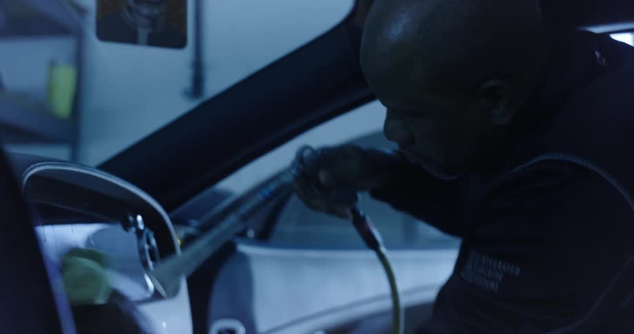 A man hoses down and wipes the interior of a car in a garage