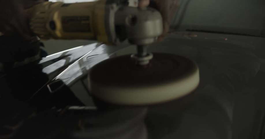 A man buffs the hood of a car with an electric buffer inside of a garage