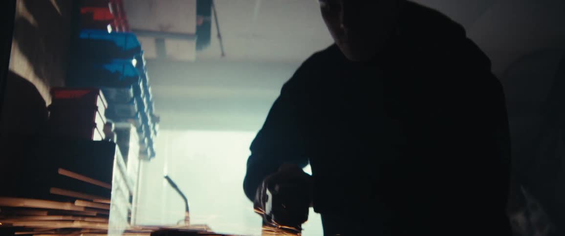 Silhouette of a person grinding metal with a power tool inside a dimly lit workshop