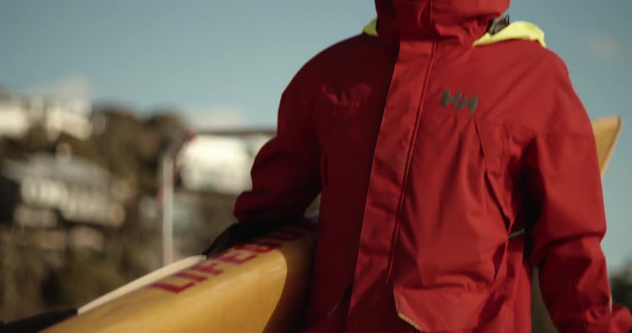 Lifeguard walking with a yellow board and wearing a red jacket