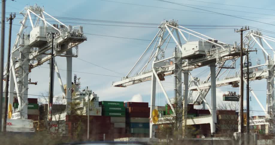 A busy port with large white cranes lifting and moving stacked shipping containers