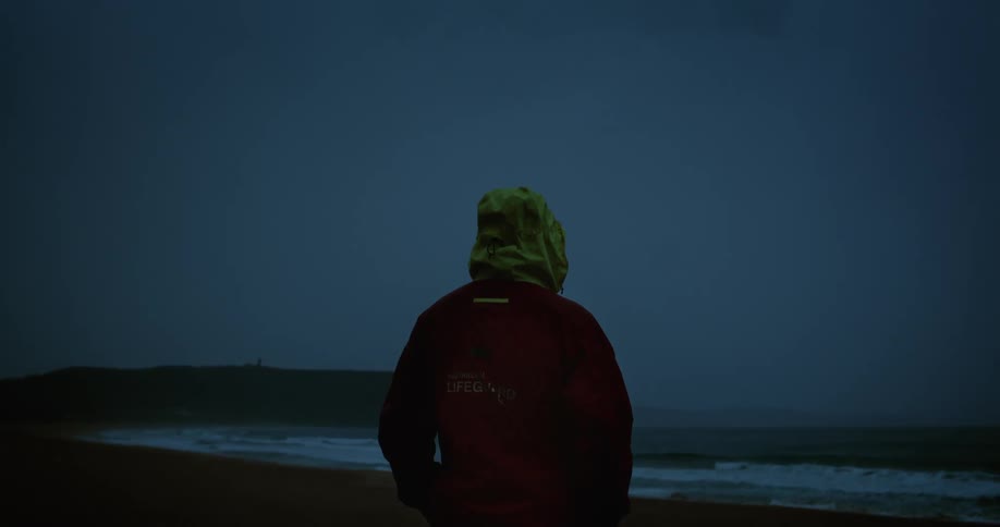 A man watches lightning shoot in the sky above the ocean