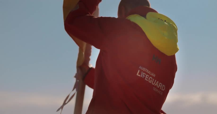 A lifeguard is planting a yellow and red flag on a beach on a sunny day