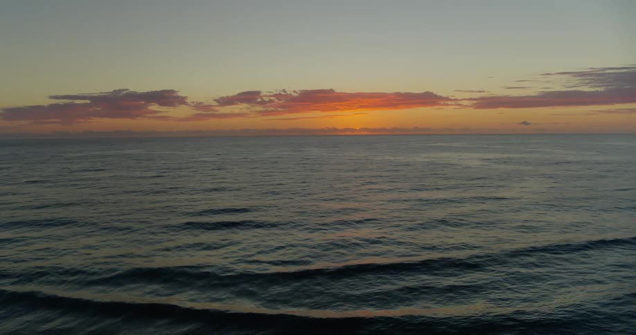 Vast ocean stretches to the horizon under a sunset sky captured from an aerial perspective