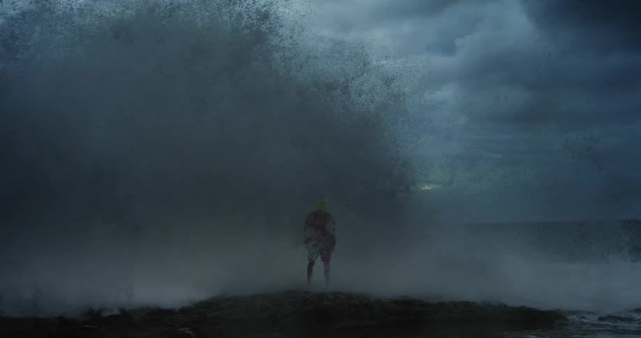 A large waves hits a man standing on the beach