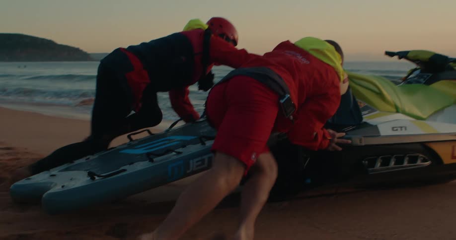 Two lifeguards putting a jet ski into the sea from the beach