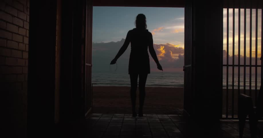 Silhouette of a woman jumping rope in a backyard facing the beach
