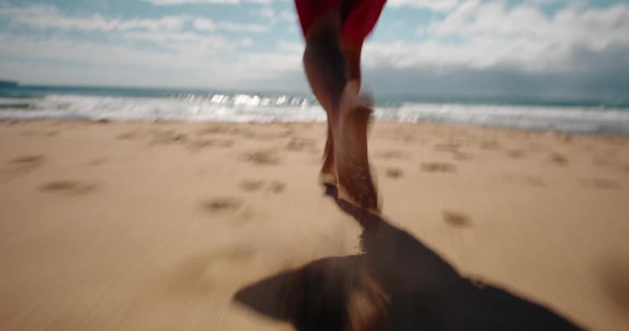 A man wearing swim trunks runs towards the ocean on the beach