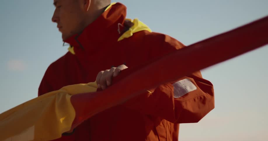 A person in a red jacket is holding and carrying a yellow and red flag against a clear blue sky