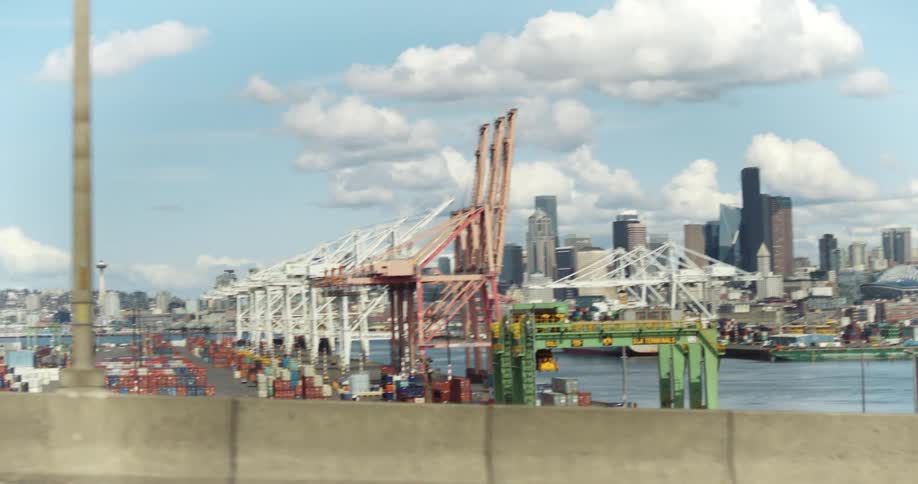 View of a port with cranes and containers with the city in the background under a blue sky with clouds
