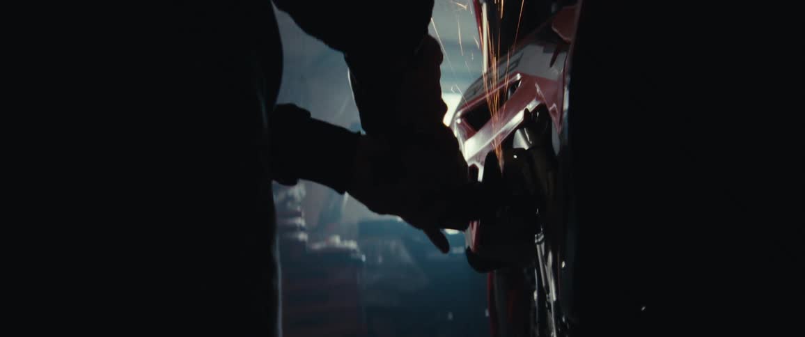 In a bike shop a mechanic uses a hand grinder on an orange dirt bike with sparks flying as camera zooms in on the grinding