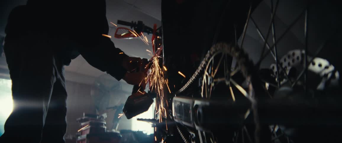 A person is using a power tool to grind or cut metal on a motorcycle causing bright sparks to fly in a workshop filled with various tools and equipment