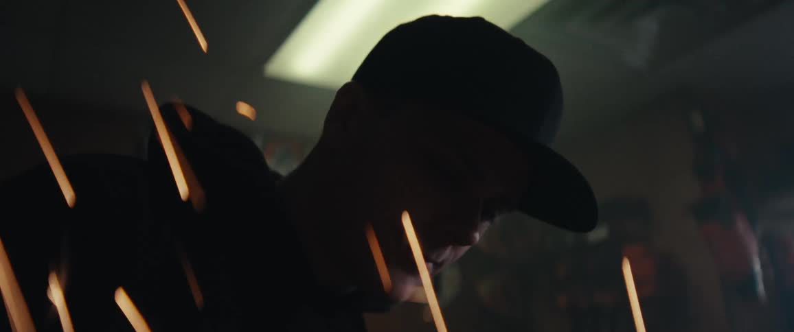 Man in cap working while metal sparks illuminate the environment
