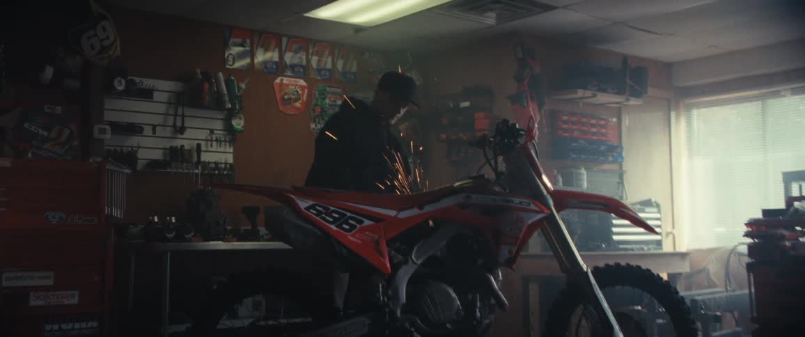 Mechanic works on an orange motocross bike inside a workshop creating sparks in the process