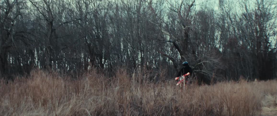 Person on a motorcycle performing stunts in tall dry grass