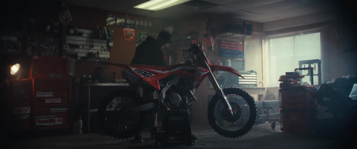 A person is using a power tool to grind or cut metal on a motorcycle causing bright sparks to fly in a workshop filled with various tools and equipment
