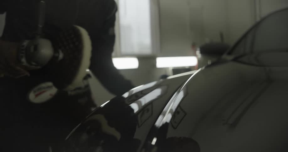 Man wiping the front hood of a black vehicle with a blue cloth