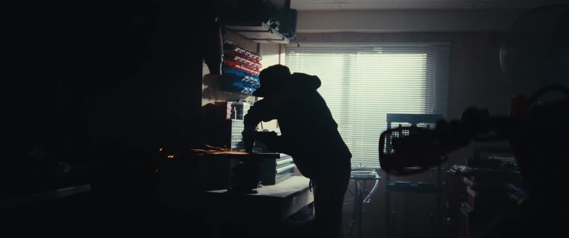 Silhouette of a man in a cap polishing a metal sheet in a workshop