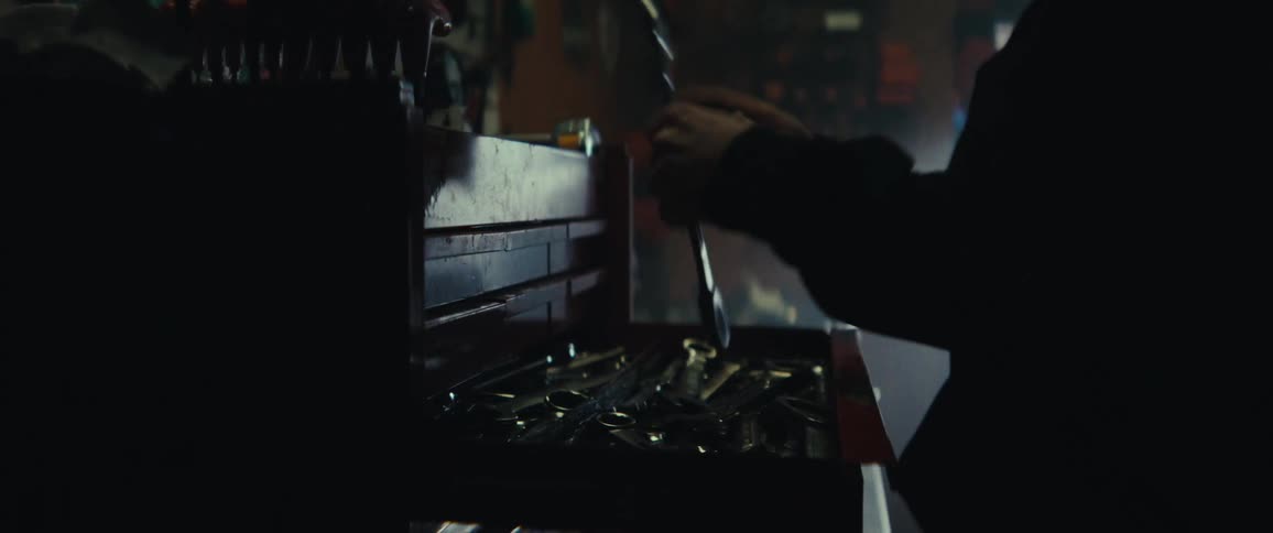 A person reaches into an open toolbox filled with various wrenches and tools inside a dimly lit workshop