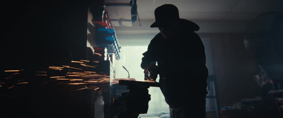 A man is cutting metal with a tool in the dark shop