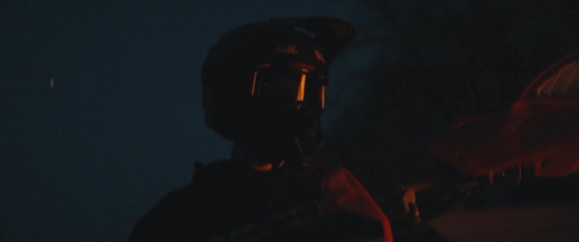A closeup view of a man wearing a motorcycle helmet looking at a campfire at night
