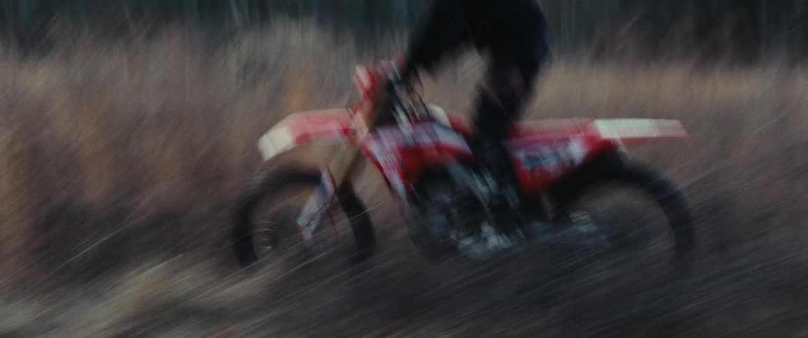 Motorcyclist in black clothing riding a red motorcycle at high speed through a rural area