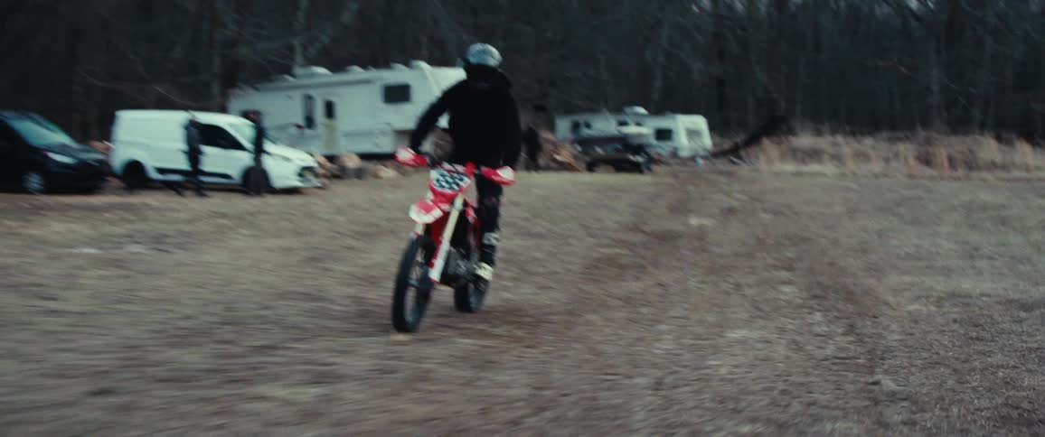 Motorcycle rider jumping off metal ramp on a dirt road then doing a wheelie in the forest