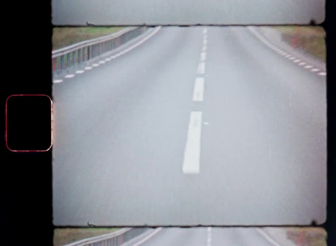 An old looking film shows the point of view of someone in a vehicle driving forward