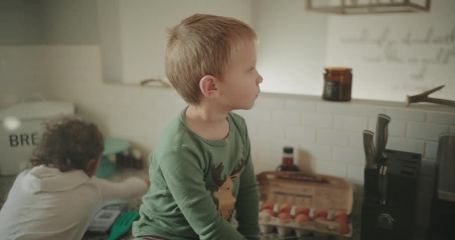 Boy sits on the kitchen counter while his sister reaches across the same counter
