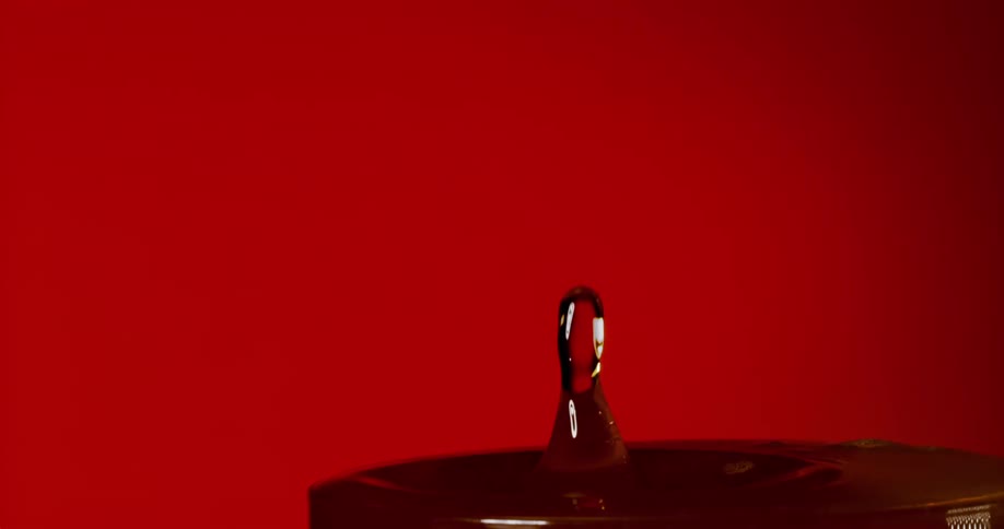 Water drop falling on a surface generating impact against a red background
