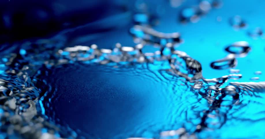 Water droplets impact a reflective surface under blue lights creating a splash and ripples