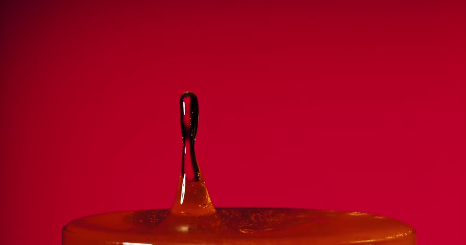A closeup shot shows a vibrant orange liquid splashing against a deep blue red