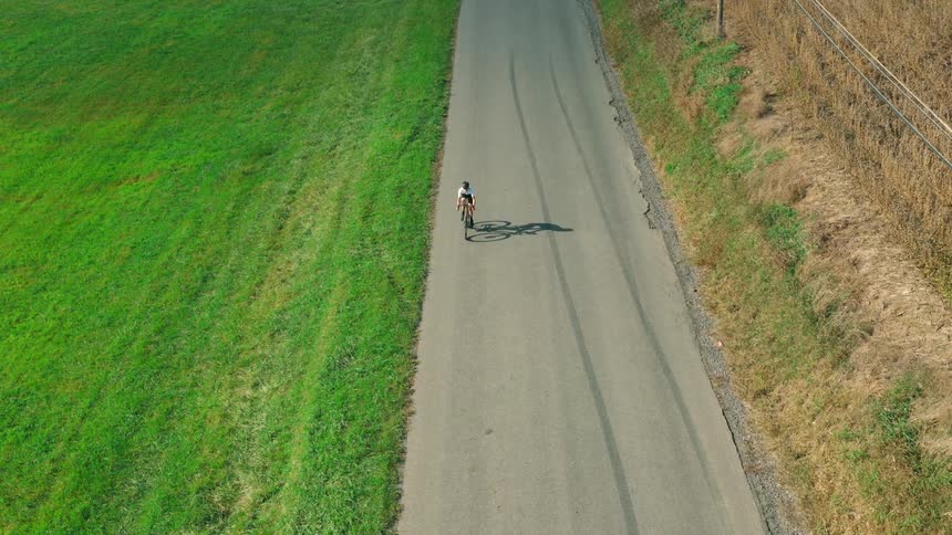 A cyclist is biking on a road surrounded by fields in the countryside