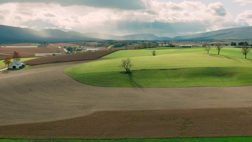 An aerial view of a farm with a large grass field surrounded by a dirt field with a white house
